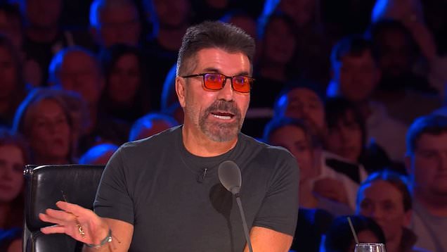 Simon Cowell speaking into a microphone on the judging panel on Britain's Got Talent. He is wearing a grey t-shirt and red sunglasses